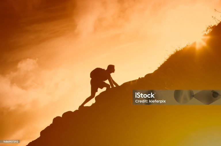 Silhouette of man climbing up a mountain